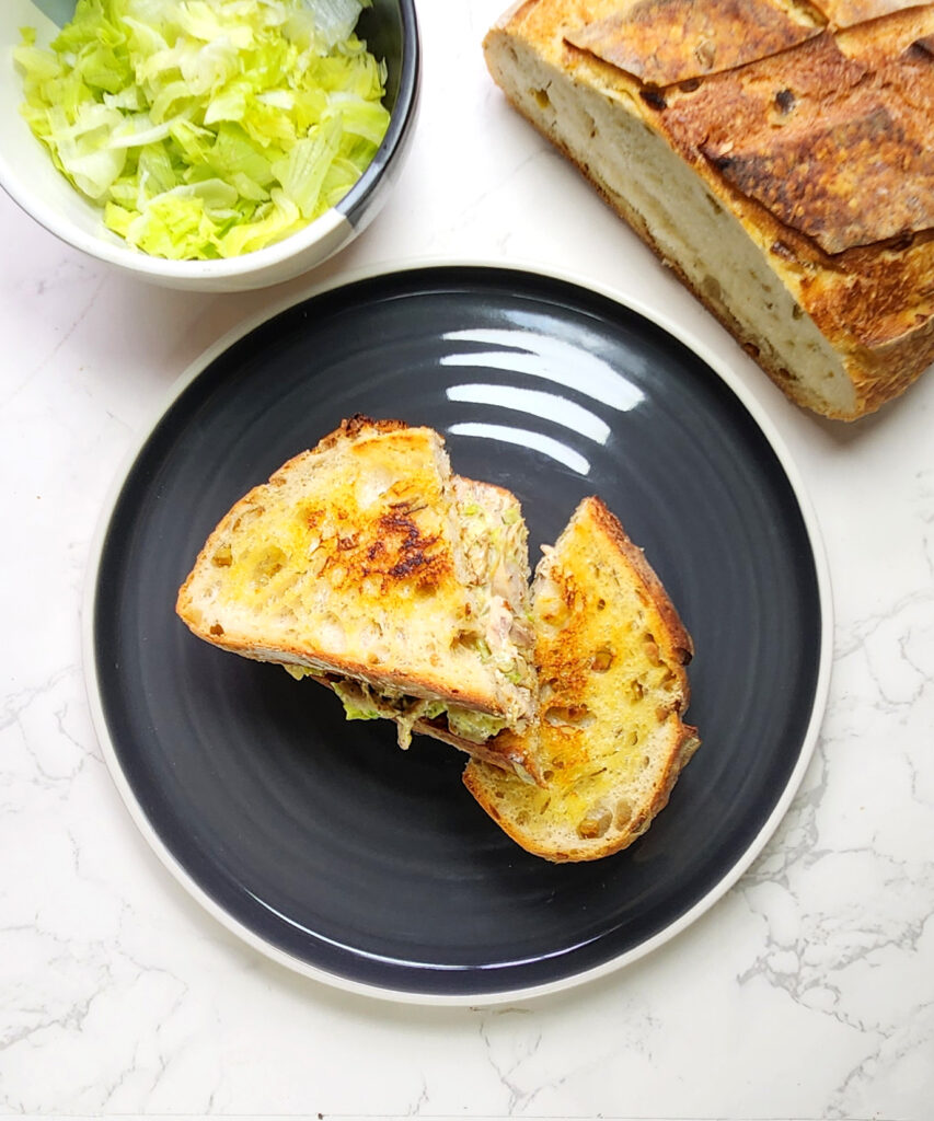 Chicken mayo sandwich on a plate with sourdough bread and shredded lettuce leaves in the background.