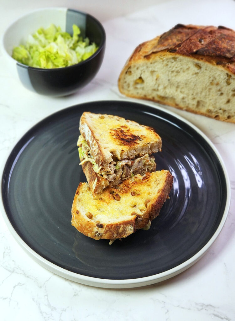 Chicken mayo sandwich on a plate with sourdough bread and shredded lettuce leaves in the background.