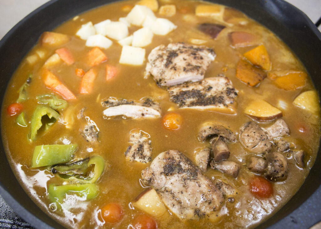 Japanese curry ingredients including vegetables, curry base and chicken bubbling in a pan