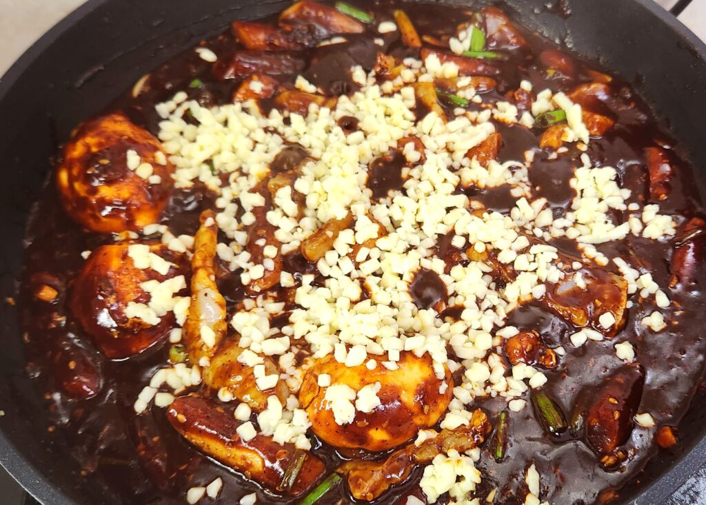 Tteokbokki in a pan, sauce bubbling with cheese melting on top.