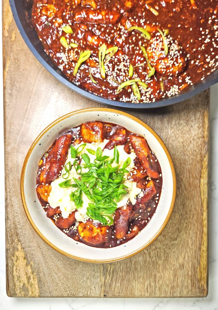 Tteokbokki in a gochujang spicy sauce in a bowl and pan with melted cheese and green onions