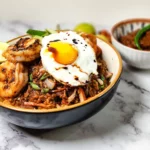 Nasi Goreng Indonesian fried rice in a bowl with prawns, cherry tomatoes, cucumbers, lime and a fried egg, sambal terasi