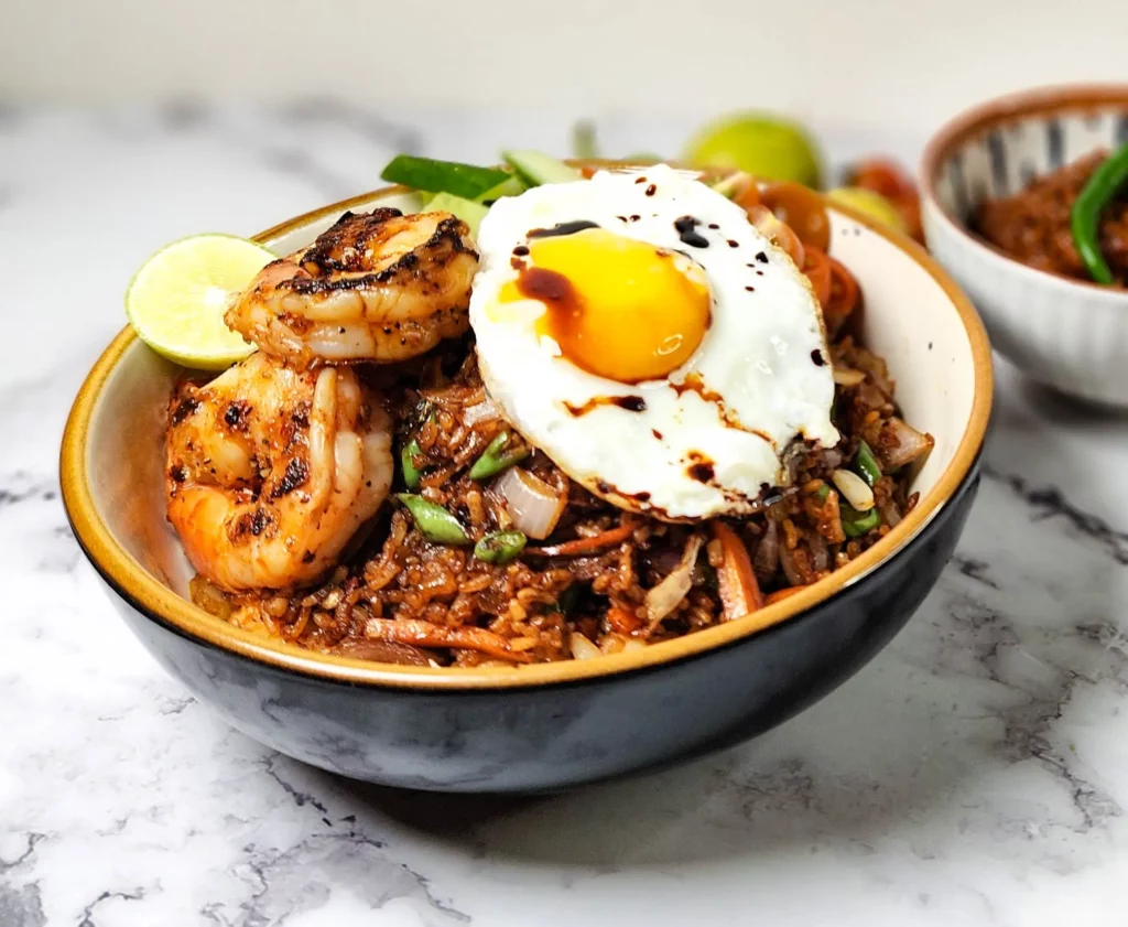 Nasi Goreng Indonesian fried rice in a bowl with prawns, cherry tomatoes, cucumbers, lime and a fried egg, sambal terasi