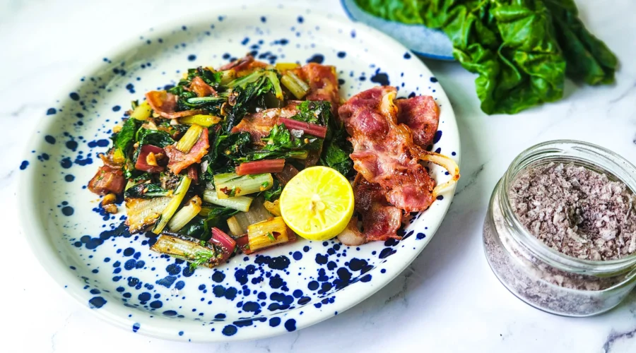 Sauteed Swiss chard with bacon on a plate with lime and salt