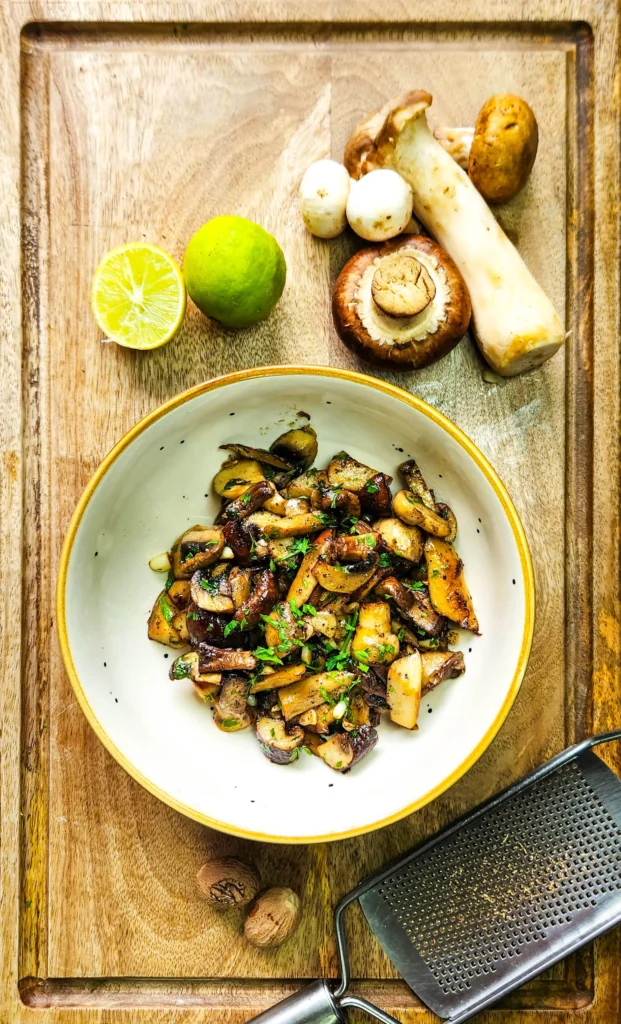 Garlic Butter Mushrooms in a plate with parsley on top, assorted mushrooms, lime and nutmeg