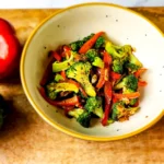 chargrilled garlic broccoli and peppers in a bowl with bell pepper, broccoli and salt on the side