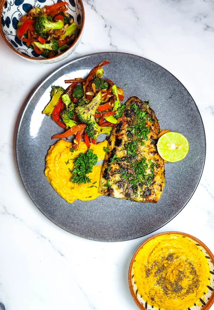 lemon butter fish with parsley on a plate with pumpkin mash and chargrilled broccoli and peppers and lime.