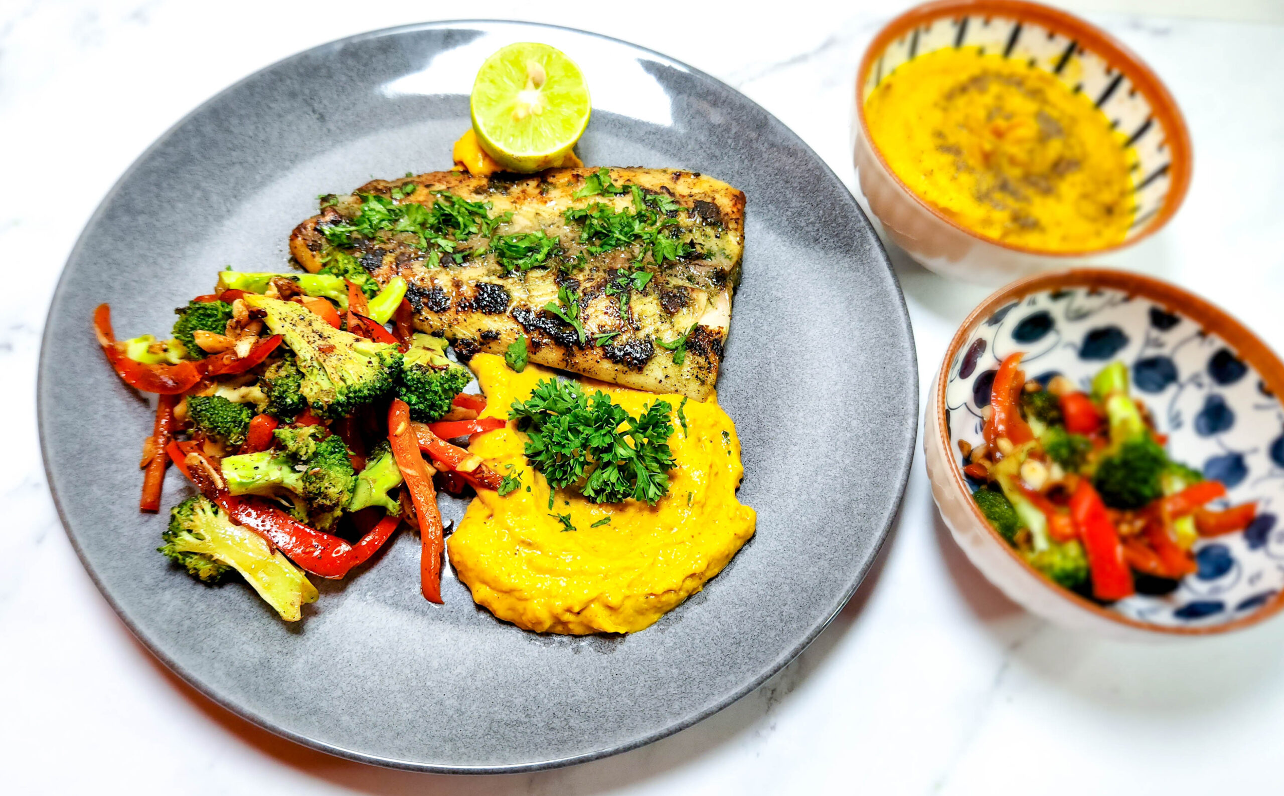 parsley butter grilled fish on a plate with pumpkin mash and chargrilled broccoli and peppers and lime.