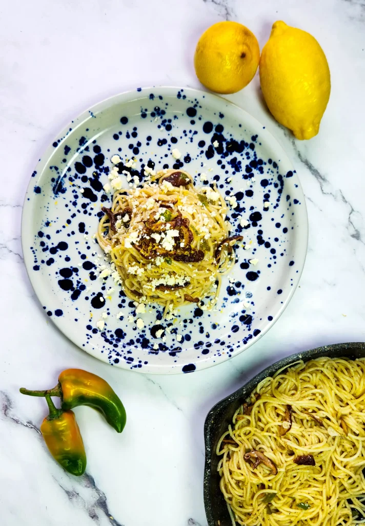 Spaghetti with lemon butter sauce in a plate with lemons, goat's cheese and shiitake mushrooms, peppers