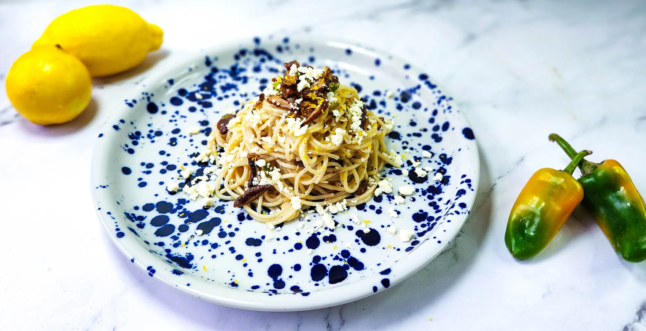 lemon butter linguine in a plate with lemons, goat's cheese and shiitake mushrooms, peppers