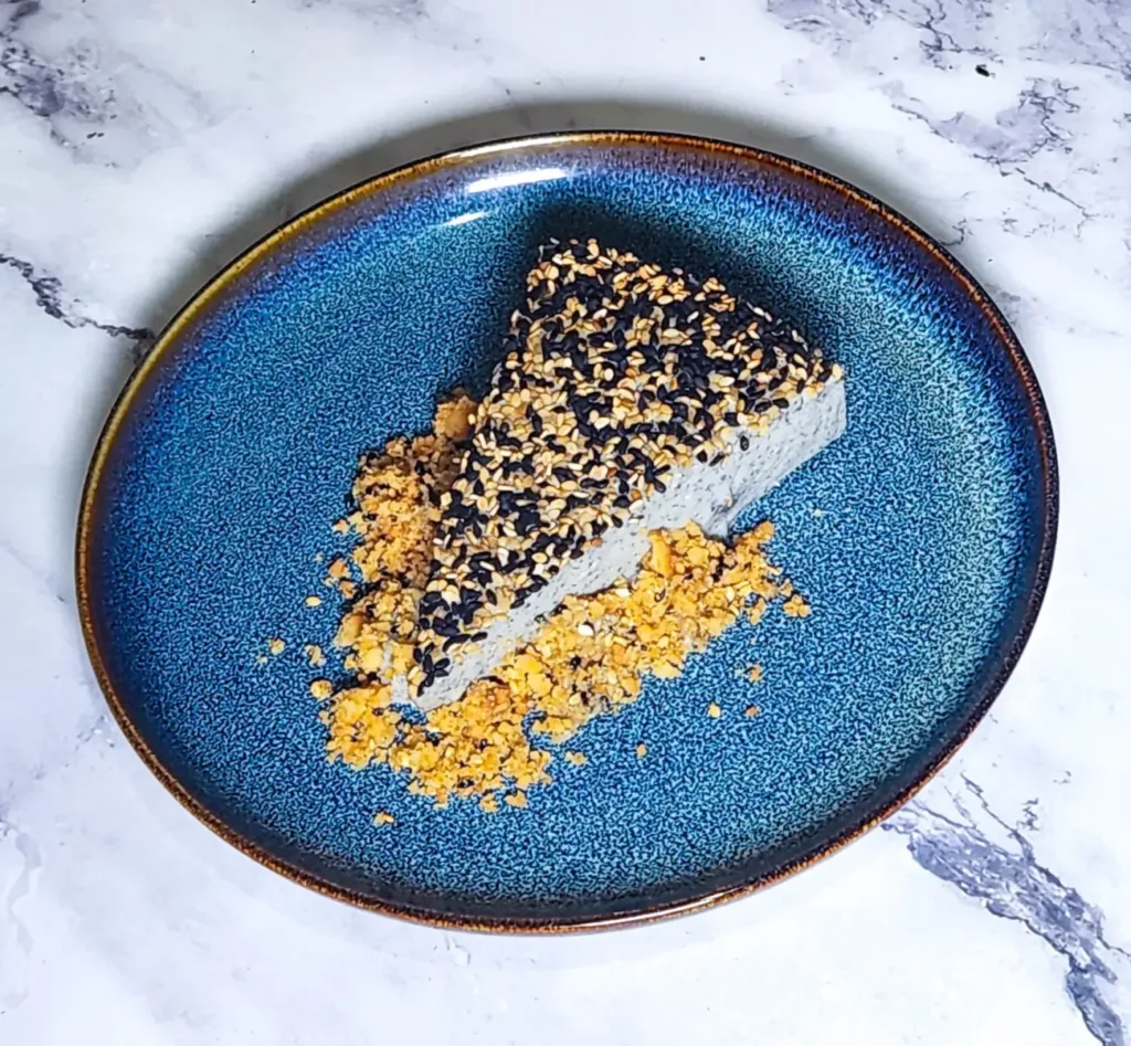 black sesame cheesecake slice on plate with biscuit base