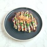 okonomiyaki on a plate, japanese savoury street food snack, pancake made with cabbage