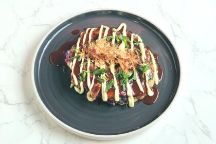 okonomiyaki on a plate, japanese savoury street food snack, pancake made with cabbage